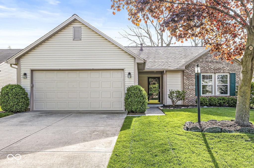 ranch-style house featuring an attached garage, roof with shingles, a front yard, and concrete driveway
