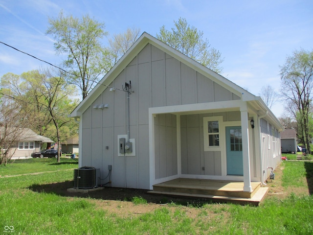 back of property with central air condition unit, board and batten siding, and a yard