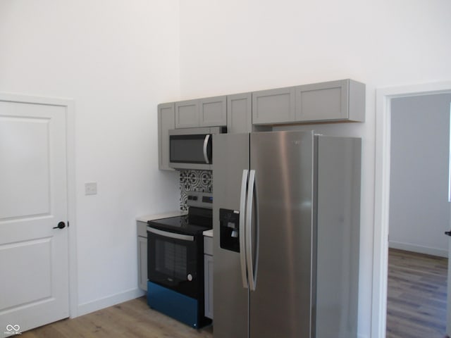 kitchen with appliances with stainless steel finishes, gray cabinetry, light wood-style floors, and baseboards