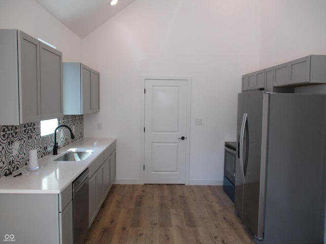 kitchen with appliances with stainless steel finishes, gray cabinets, a sink, tasteful backsplash, and high vaulted ceiling