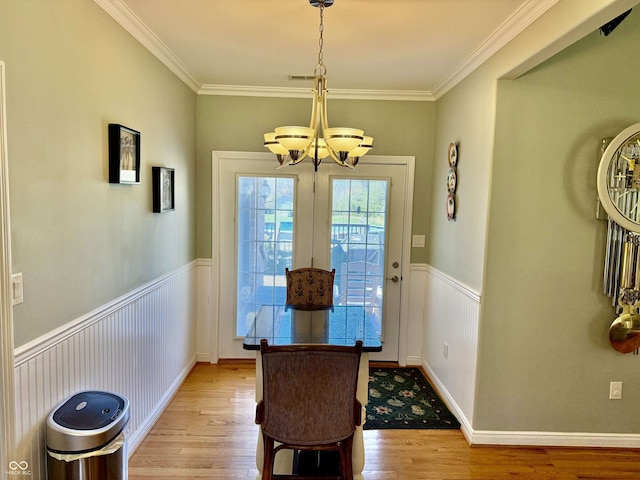 dining space featuring a notable chandelier, a wainscoted wall, crown molding, and light wood-style flooring