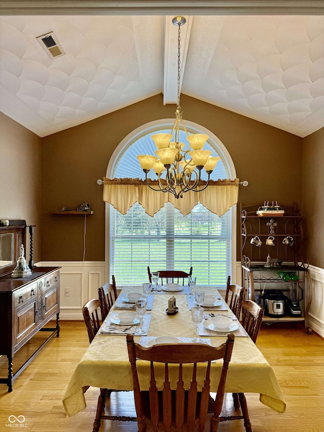 dining area featuring wood finished floors, vaulted ceiling with beams, a notable chandelier, and a wainscoted wall