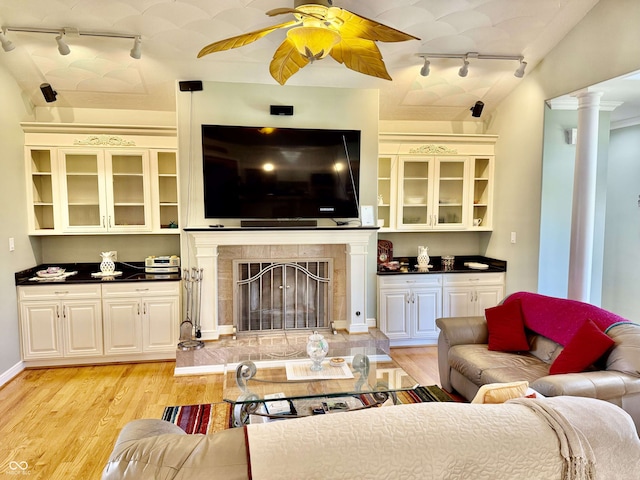 living area with rail lighting, a ceiling fan, light wood-type flooring, and decorative columns