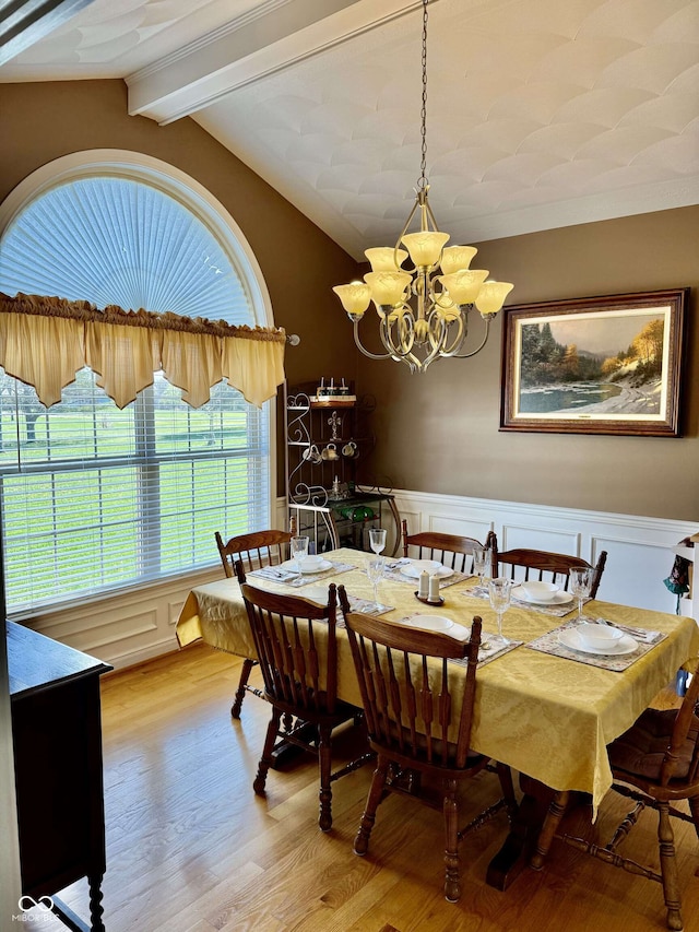dining room with lofted ceiling with beams, wainscoting, a notable chandelier, wood finished floors, and a decorative wall