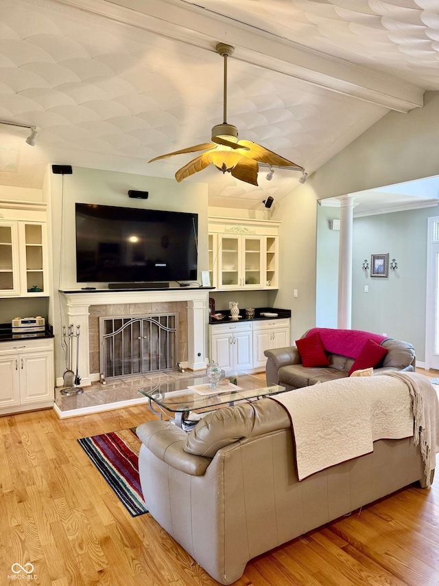living room featuring light wood finished floors, vaulted ceiling with beams, a fireplace with raised hearth, and ceiling fan