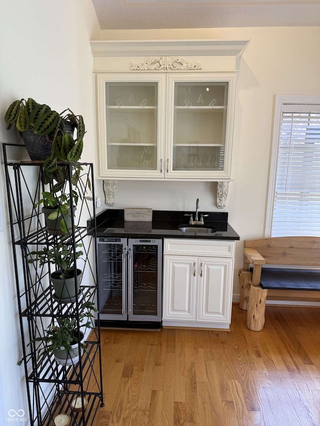 bar featuring indoor wet bar, light wood-type flooring, a sink, and wine cooler