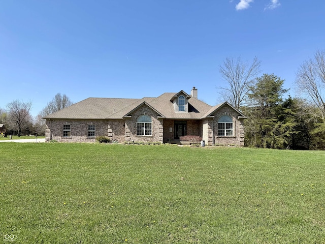 view of front of home featuring a chimney, brick siding, and a front yard