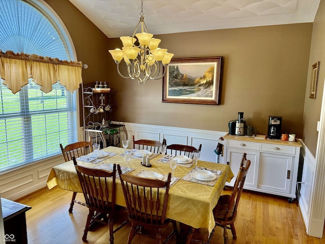 dining room with a wainscoted wall, vaulted ceiling, light wood-type flooring, a decorative wall, and a chandelier