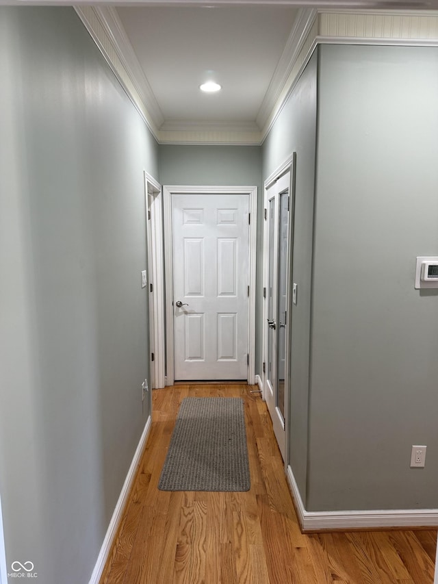 hallway featuring light wood finished floors, baseboards, and crown molding