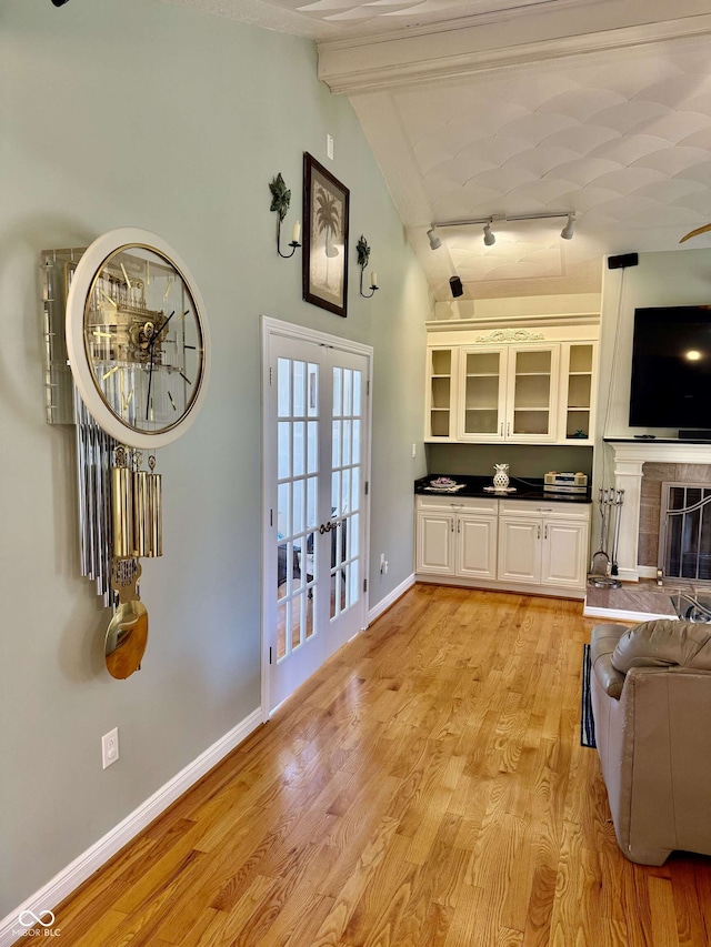 interior space featuring french doors, beam ceiling, baseboards, glass insert cabinets, and rail lighting