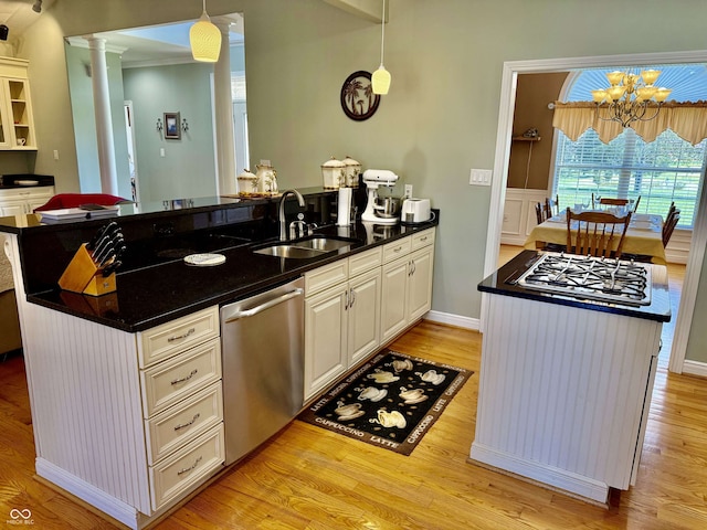kitchen with a sink, hanging light fixtures, light wood-style floors, a peninsula, and appliances with stainless steel finishes