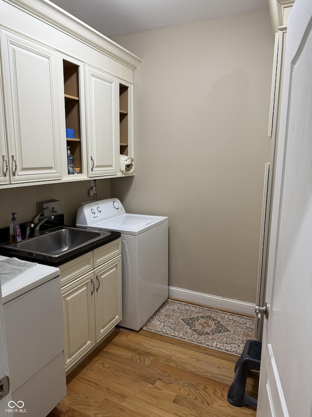 clothes washing area with light wood-style flooring, a sink, baseboards, cabinet space, and washer and dryer