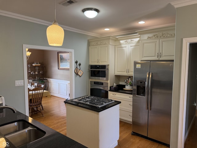 kitchen featuring light wood finished floors, a sink, dark countertops, appliances with stainless steel finishes, and ornamental molding