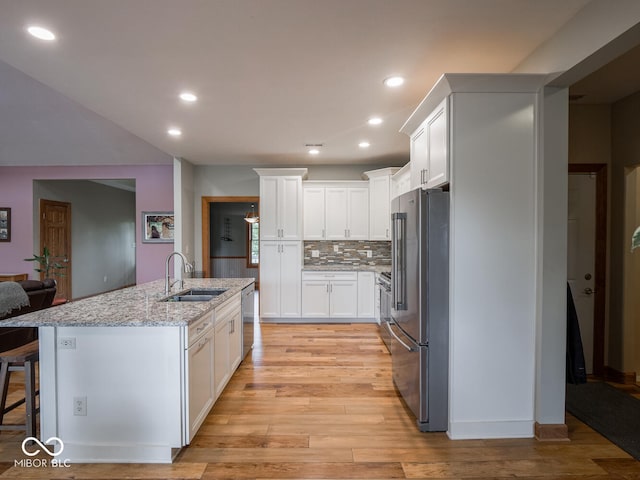 kitchen with appliances with stainless steel finishes, a sink, white cabinetry, light stone counters, and light wood-style flooring