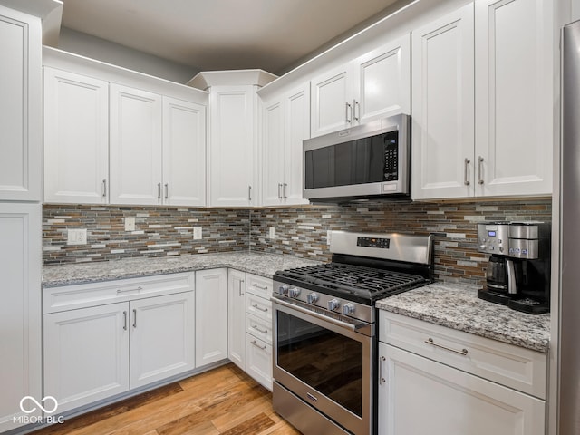 kitchen featuring stainless steel appliances, white cabinets, decorative backsplash, light wood-style floors, and light stone counters