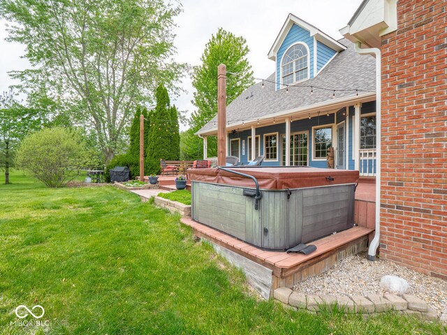 rear view of property featuring a hot tub, a lawn, a shingled roof, brick siding, and a deck