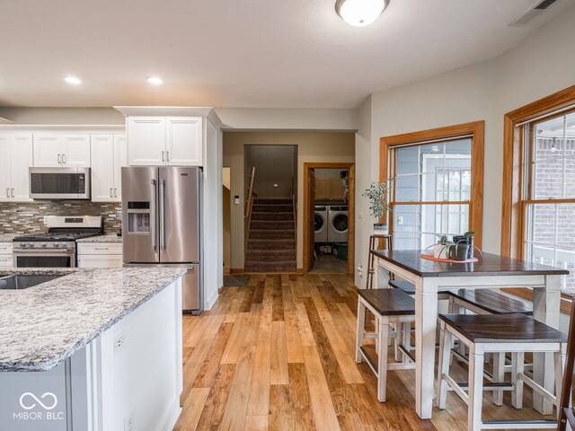 kitchen featuring stainless steel appliances, washer and clothes dryer, white cabinets, light wood-style flooring, and decorative backsplash