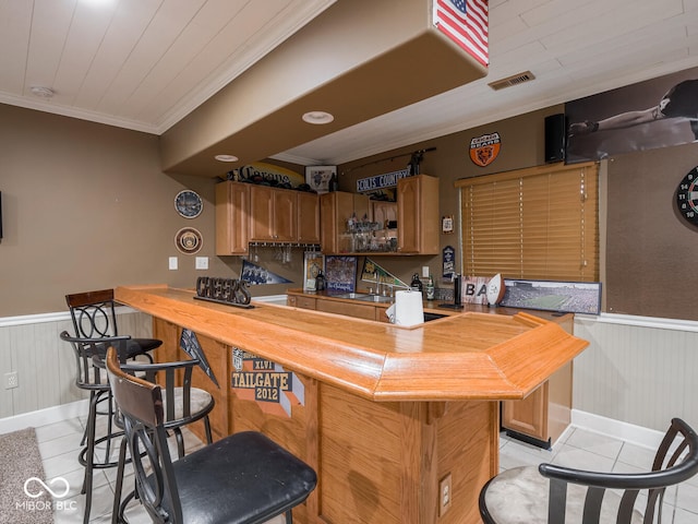 indoor dry bar with light tile patterned floors, a wainscoted wall, and ornamental molding