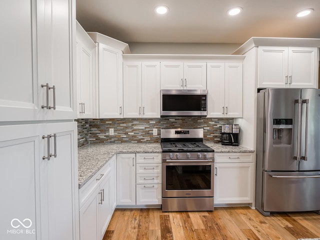 kitchen with appliances with stainless steel finishes, white cabinets, backsplash, light stone countertops, and recessed lighting