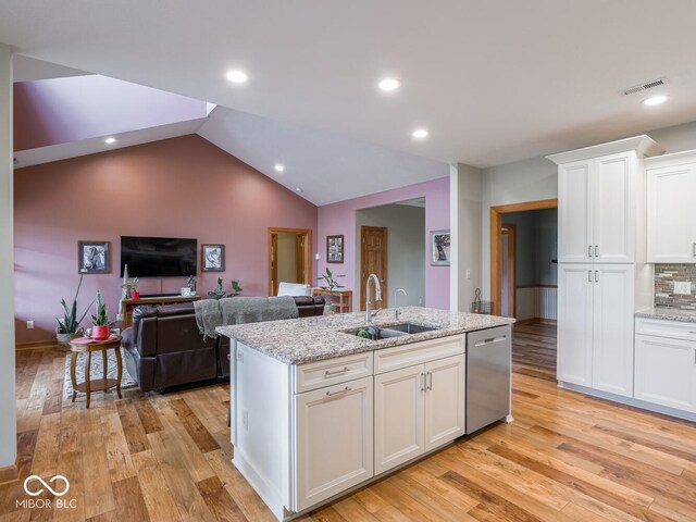 kitchen with a sink, dishwasher, white cabinets, light wood-style floors, and a kitchen island with sink