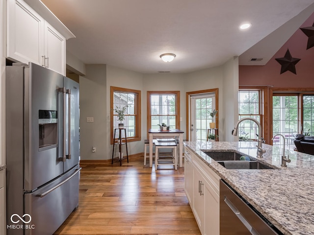 kitchen with appliances with stainless steel finishes, a sink, light wood-type flooring, white cabinets, and recessed lighting