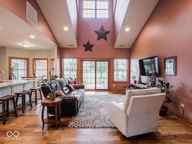 living area featuring healthy amount of natural light, light wood-style floors, a towering ceiling, recessed lighting, and baseboards