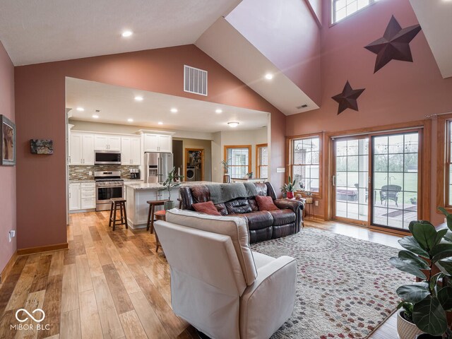 living area featuring high vaulted ceiling, light wood-style floors, and recessed lighting