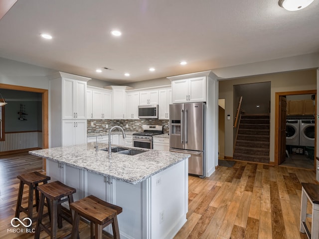 kitchen with stainless steel appliances, a sink, washing machine and clothes dryer, light wood finished floors, and white cabinetry