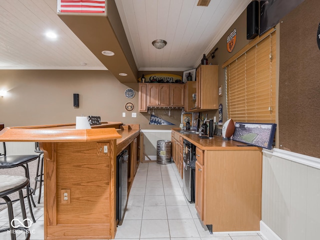 kitchen featuring crown molding, light tile patterned flooring, a sink, a wainscoted wall, and dishwashing machine