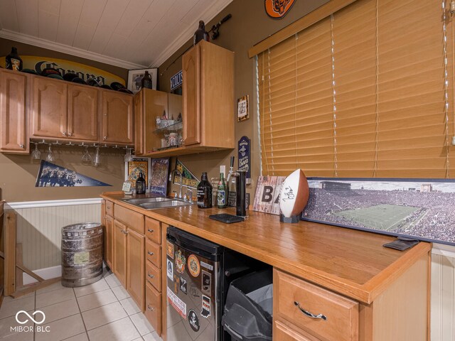 bar area featuring a sink, crown molding, light tile patterned flooring, and wainscoting