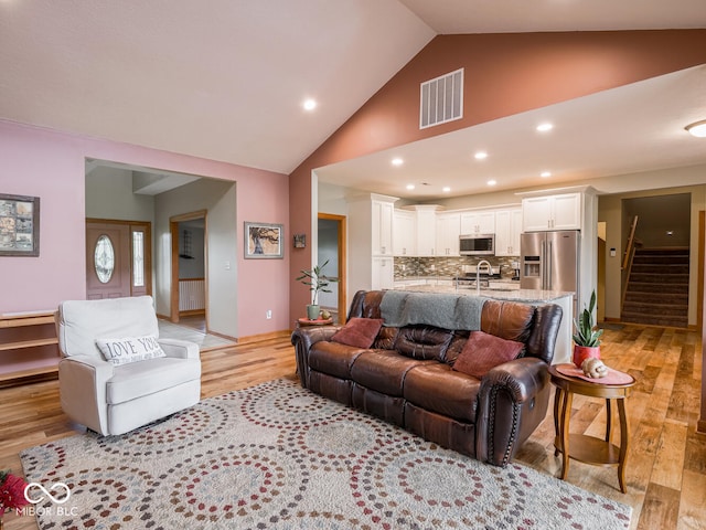 living area featuring light wood-style floors, stairs, high vaulted ceiling, and recessed lighting