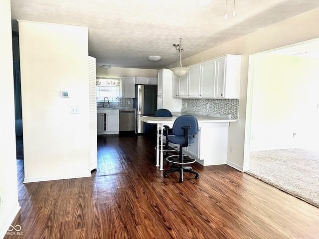 kitchen with a kitchen breakfast bar, decorative backsplash, a sink, stainless steel appliances, and dark wood finished floors