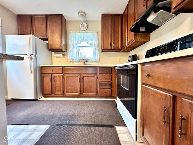 kitchen featuring freestanding refrigerator, brown cabinetry, light countertops, carpet, and range hood