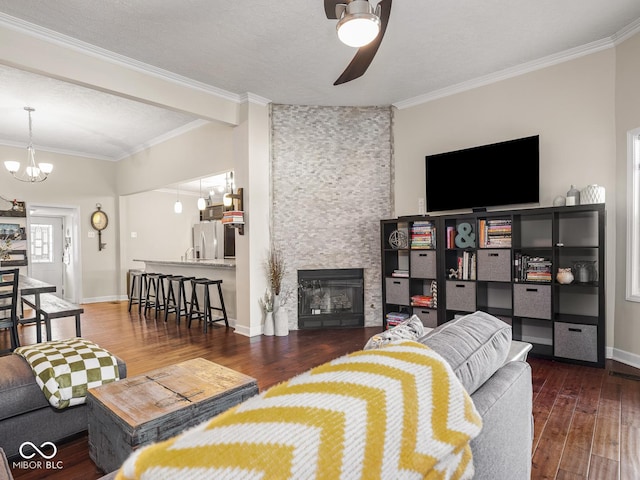 living room with a stone fireplace, crown molding, ceiling fan with notable chandelier, and hardwood / wood-style flooring