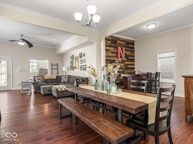 dining room with dark wood-style flooring, a textured ceiling, crown molding, baseboards, and ceiling fan with notable chandelier