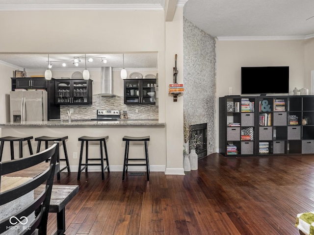 kitchen featuring appliances with stainless steel finishes, glass insert cabinets, wall chimney exhaust hood, and a kitchen bar