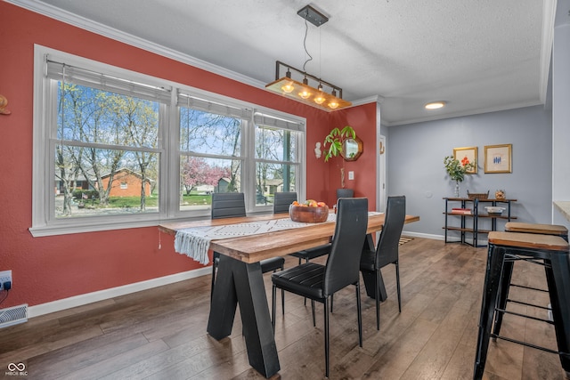 dining space featuring a textured ceiling, hardwood / wood-style flooring, baseboards, ornamental molding, and visible vents