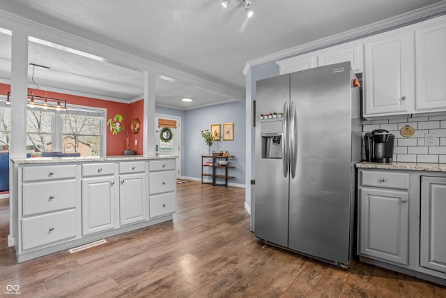 kitchen with tasteful backsplash, visible vents, wood finished floors, crown molding, and stainless steel fridge with ice dispenser