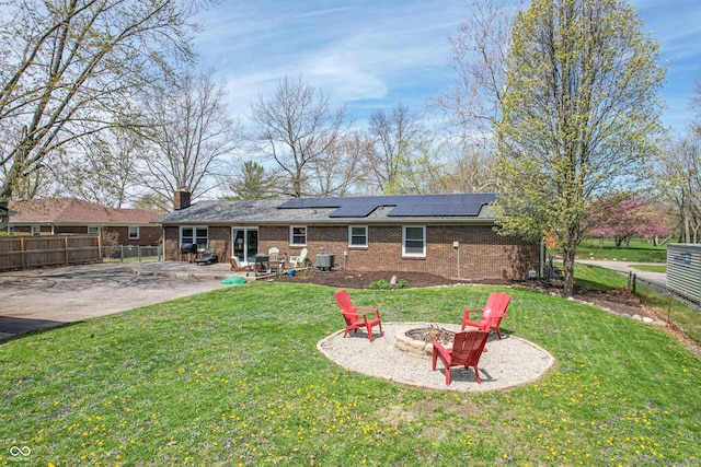 rear view of house with a lawn, a fire pit, a patio, solar panels, and brick siding