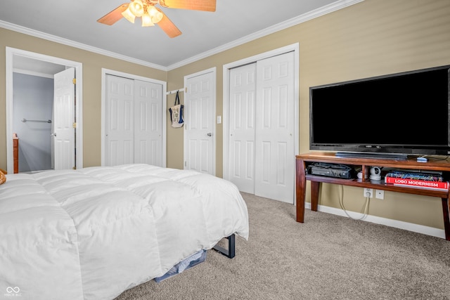carpeted bedroom featuring a ceiling fan, crown molding, two closets, baseboards, and ensuite bath