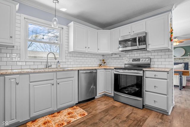 kitchen featuring crown molding, wood finished floors, a sink, white cabinetry, and appliances with stainless steel finishes