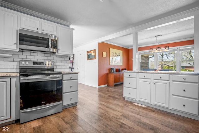 kitchen featuring stainless steel appliances, wood finished floors, ornamental molding, baseboards, and decorative backsplash