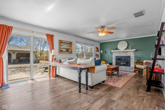 living area with wood finished floors, visible vents, a ceiling fan, ornamental molding, and a fireplace