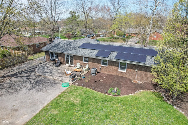 exterior space with a patio area, a lawn, brick siding, and solar panels