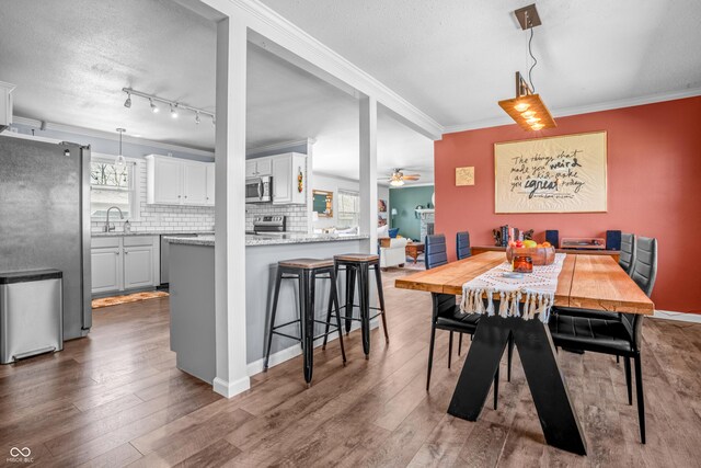 dining area featuring a ceiling fan, a textured ceiling, ornamental molding, and dark wood-style flooring