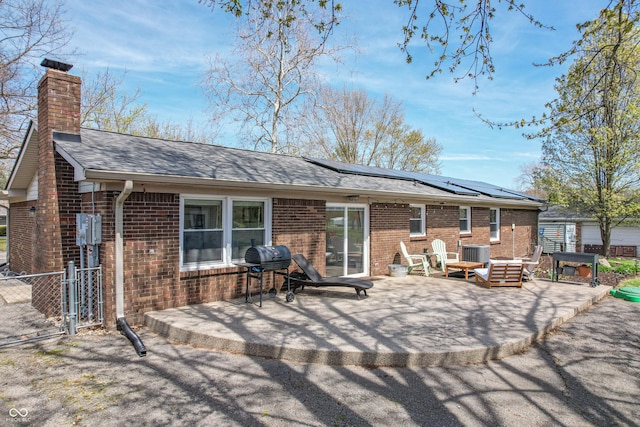 rear view of house with central AC unit, solar panels, a chimney, brick siding, and a patio