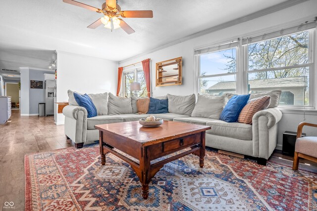 living room featuring ceiling fan, baseboards, crown molding, and wood finished floors