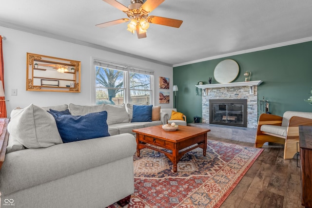 living area with a ceiling fan, a stone fireplace, dark wood-type flooring, and ornamental molding