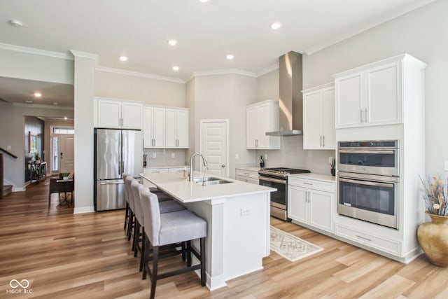 kitchen with an island with sink, stainless steel appliances, wall chimney range hood, a sink, and a kitchen breakfast bar