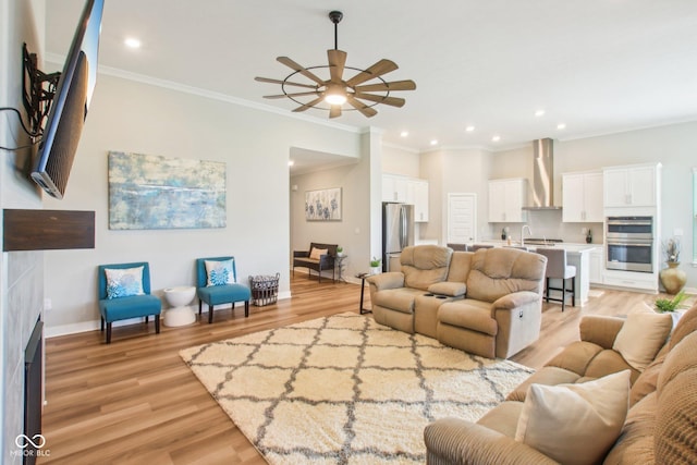 living room featuring recessed lighting, baseboards, light wood-type flooring, a ceiling fan, and crown molding